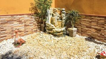 A garden with a rock waterfall, pebbles, a statue of a goose, and a mushroom.