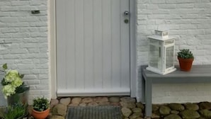 Een witte deur met een rond raam, een kleine bloempot en een lantaarn op een plank.