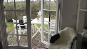 Een kamer met een grote schuifglazen deur die leidt naar een terras buiten, met een witte stoel en een tafel.