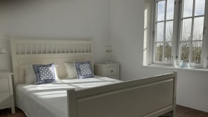 Een wit bed met hoofdeinde, twee nachtkastjes en een raam met uitzicht.
