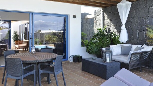 An outdoor patio with a round table and chairs, a cushioned seating area, and a stone wall. - Villa Bella Vista Blu (Yaiza)