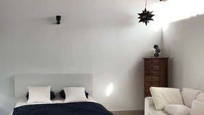 A minimalist bedroom with a bed, a white sofa, and a wooden dresser. - Villa Bella Vista Blu (Yaiza)