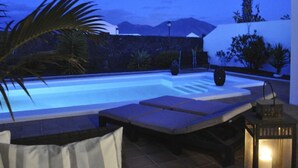 A swimming pool with lounge chairs and a stone wall. - Villa Bella Vista Blu (Yaiza)