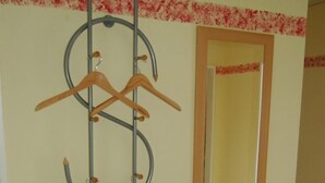 A room with a wooden cabinet, a mirror, and a metal rack with wooden hangers. - Ferienwohnung Rottmann, 1-4 Pers (Warendorf-Einen)