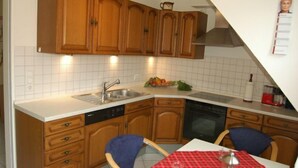 A kitchen with wooden cabinets, a sink, a dishwasher, and a table with a red checkered tablecloth. - Ferienwohnung Rottmann, 1-4 Pers (Warendorf-Einen)