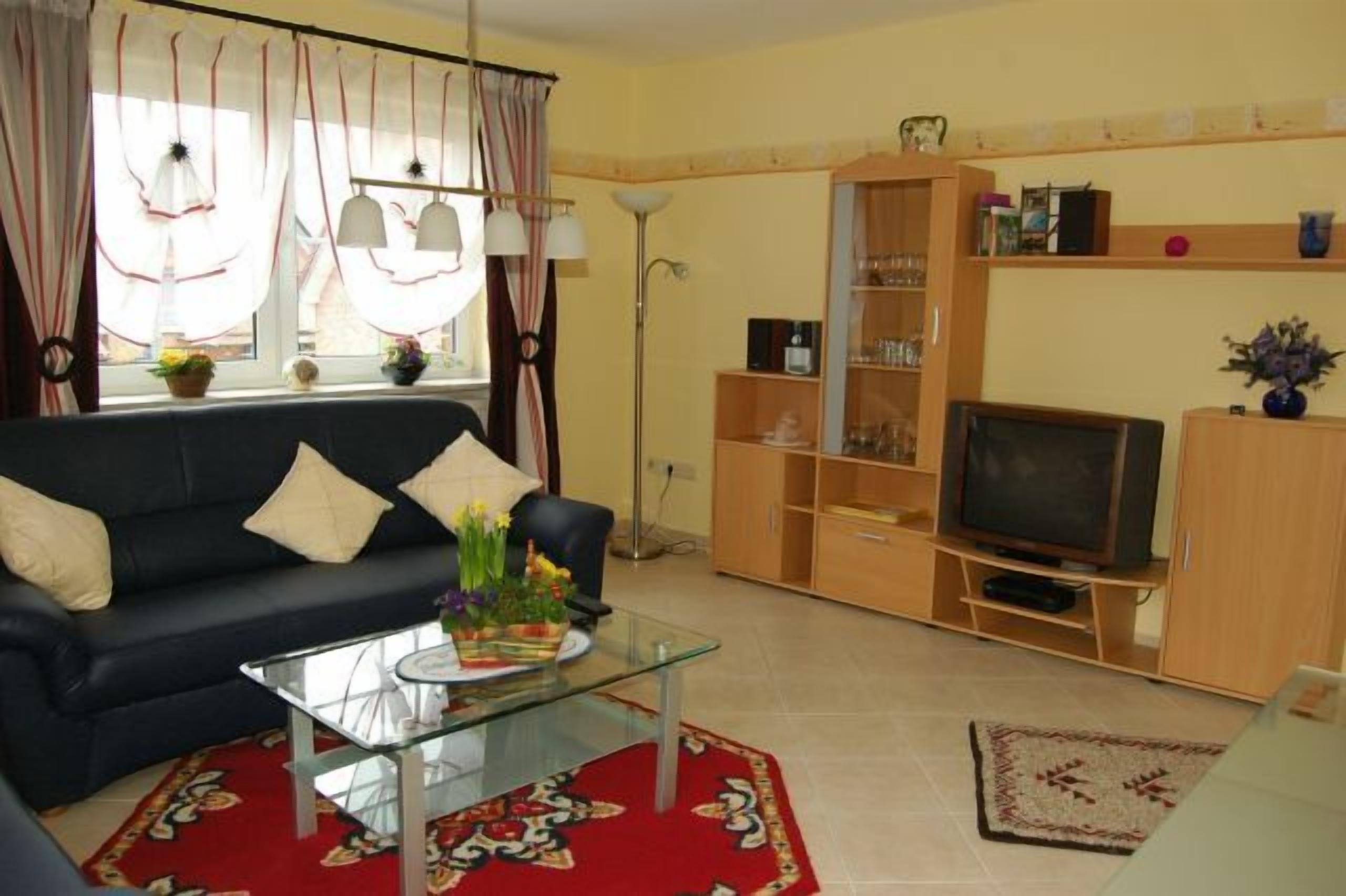 A living room with a sofa, TV, glass coffee table, and a red patterned rug.