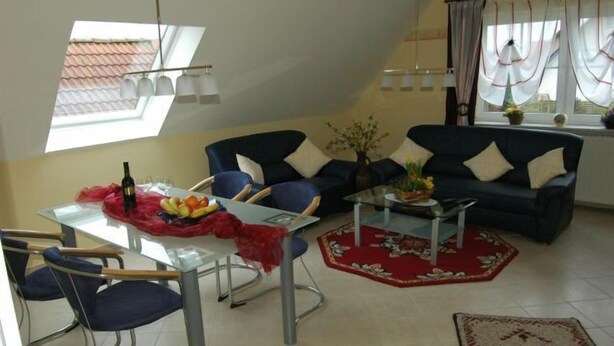 A modern living room with a glass dining table, blue chairs, a dark blue sofa, and a red rug. - Ferienwohnung Rottmann, 1-4 Pers (Warendorf-Einen)