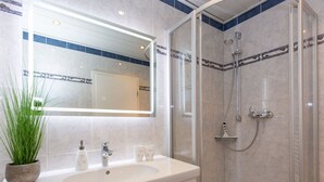 Een badkamer met een grote spiegel, een wastafel, een douche en een plant in een pot.