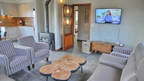 A living room with a fireplace, a television, and a kitchen in the background. - Villa in Durbuy With Ardennes Views (Durbuy)