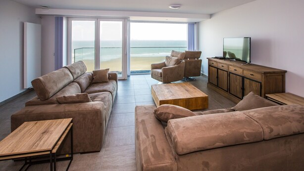 A modern living room with a sofa set, a wooden coffee table, and a TV on a wooden cabinet. - Beautiful Apartment With Phenomenal sea View (Middelkerke)
