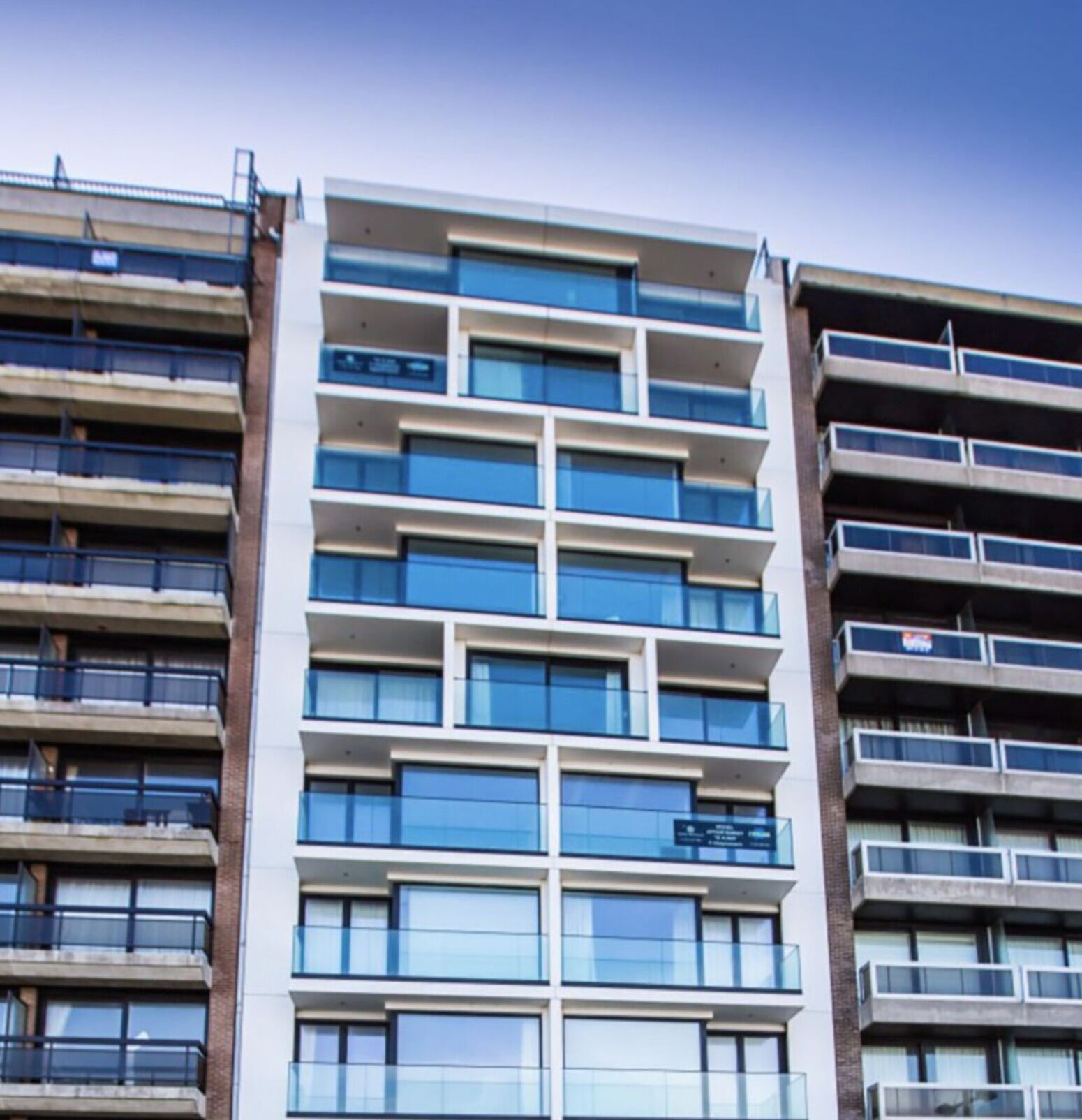 A multi-story building with a modern architectural design, featuring a mix of glass and concrete facades, and multiple balconies.