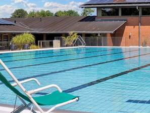 A swimming pool with clear blue water, surrounded by a brick building with a metal roof and solar panels. - 6 Person Holiday Park Home in Gilleleje (Gilleleje)