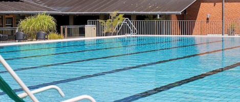 A swimming pool with clear lanes, a green pool chair, and a building with solar panels in the background.