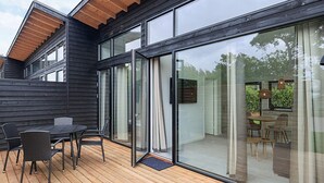 A modern house with a wooden deck, large sliding glass doors, and a dining area with outdoor furniture. - 6 Person Holiday Park Home in Gilleleje (Gilleleje)