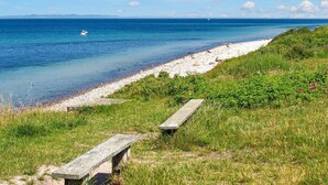 A coastal scene with a pebble beach, grassy areas, and a wooden bench. - 6 Person Holiday Park Home in Gilleleje (Gilleleje)