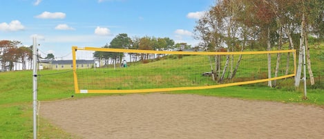 A volleyball net in a sandy area with a grassy field and trees in the background.