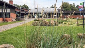 A building with a brick facade, a covered outdoor seating area, and a grassy courtyard with rocks. - 6 Person Holiday Park Home in Gilleleje (Gilleleje)