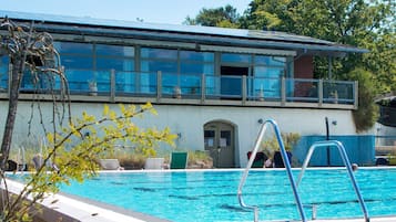 A swimming pool with a metal ladder, a yoga door, and a building with large windows and a balcony.