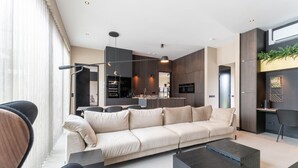 Un salon moderne avec un canapé, une table basse et des fauteuils. Il y a également un coin cuisine avec une table à manger et des chaises.