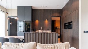 Une cuisine moderne dotée d’un îlot central, d’appareils électroménagers intégrés et d’un coin repas avec une chaise noire.
