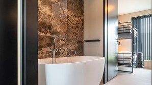 Une salle de bain moderne avec une baignoire sur pieds, un mur en marbre et un lit superposé dans la pièce adjacente.