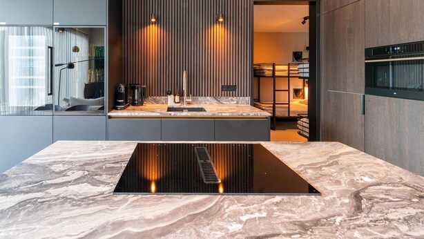 Une cuisine moderne dotée d’un îlot central, d’appareils électroménagers intégrés et offrant une vue sur l’extérieur.