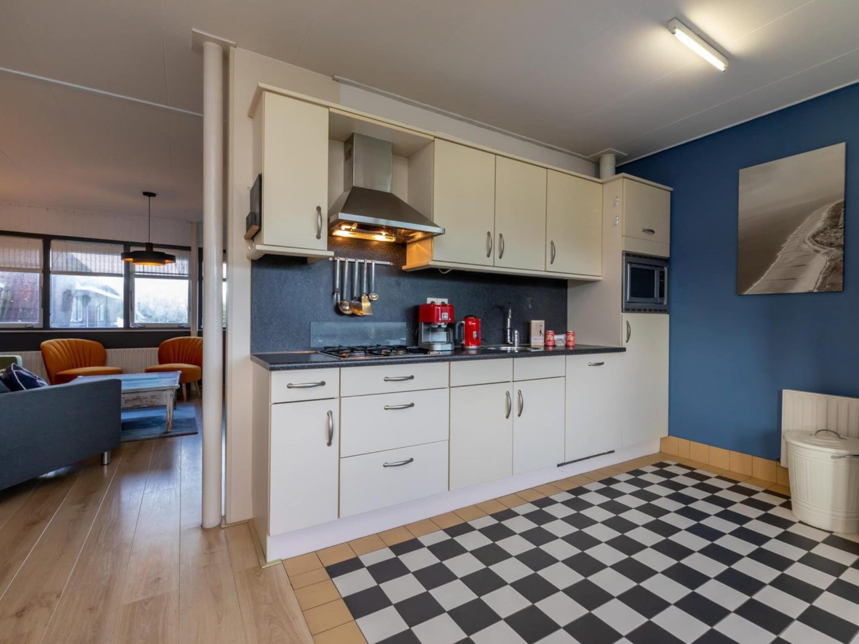 A modern kitchen with white cabinets, a gas stove, and a microwave. There is a checkered floor and a blue wall with a painting.