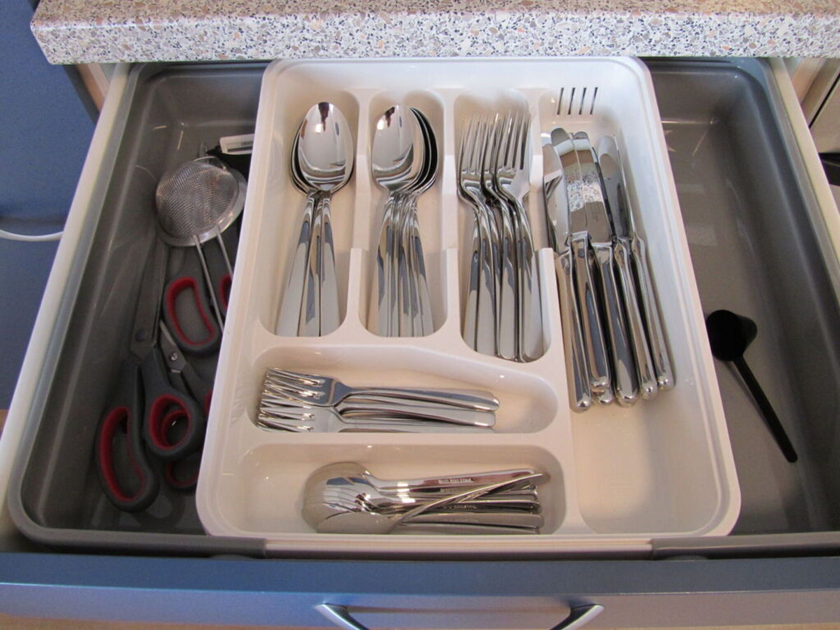 Un cajón con varios utensilios de cocina, incluyendo cucharas, tenedores y un colador.