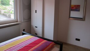 A bedroom with a bed, a window, a wardrobe, and a framed picture on the wall. - Holiday Apartment Heitmann (Hilders)