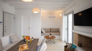 Een moderne woonkamer met een houten eettafel, witte stoelen, een bank, een klein rond salontafeltje en een open haard.