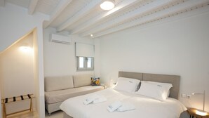 Een moderne hotelkamer met een groot bed, een kleinere bank, een houten rek en een nachtkastje met een lamp.