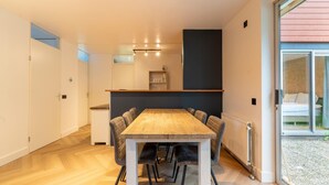 A modern kitchen with a wooden table and chairs, a built-in oven, and a large window with a view of the outside. - Holiday Home in South Holland With Shared Pool (Zevenhuizen)
