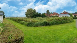 A grassy field with a pathway leading to a row of houses with red roofs. - Holiday Home in South Holland With Shared Pool (Zevenhuizen)
