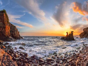 A rocky coastline with waves crashing against the shore and a sunset in the background. - 8 Person Holiday Home in Allinge (Allinge)