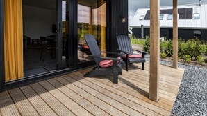 A modern outdoor deck with two Adirondack chairs, a wooden pergola, and a glass door leading to an interior space.