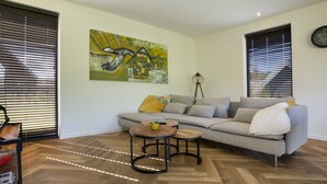A living room with a sectional sofa, two small round tables, and a painting on the wall.