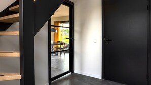 A modern interior with a staircase, a dark door, and a view into a dining area with natural light.