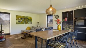 A modern kitchen with a wooden dining table, black chairs, and a yellow vase with flowers.