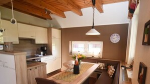 A modern kitchen with wooden cabinets, a dining area with a bench, and a large window. - Holiday Home Nispel Comfortable Vacation Home (Dornum)