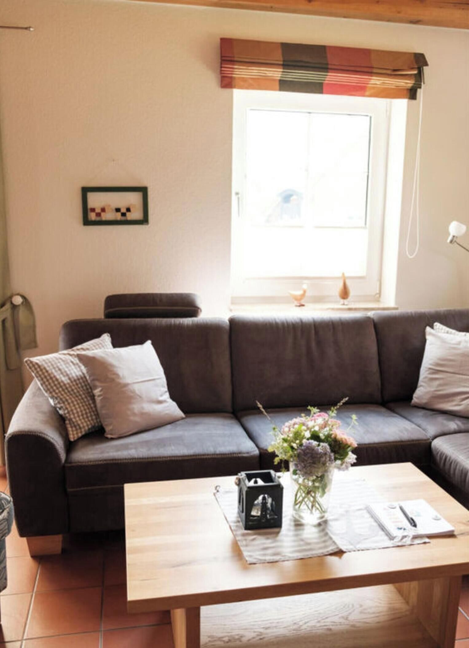 Ein Wohnzimmer mit einem braunen Sofa, einem Holztisch und einem Fenster mit einem karierten Vorhang.