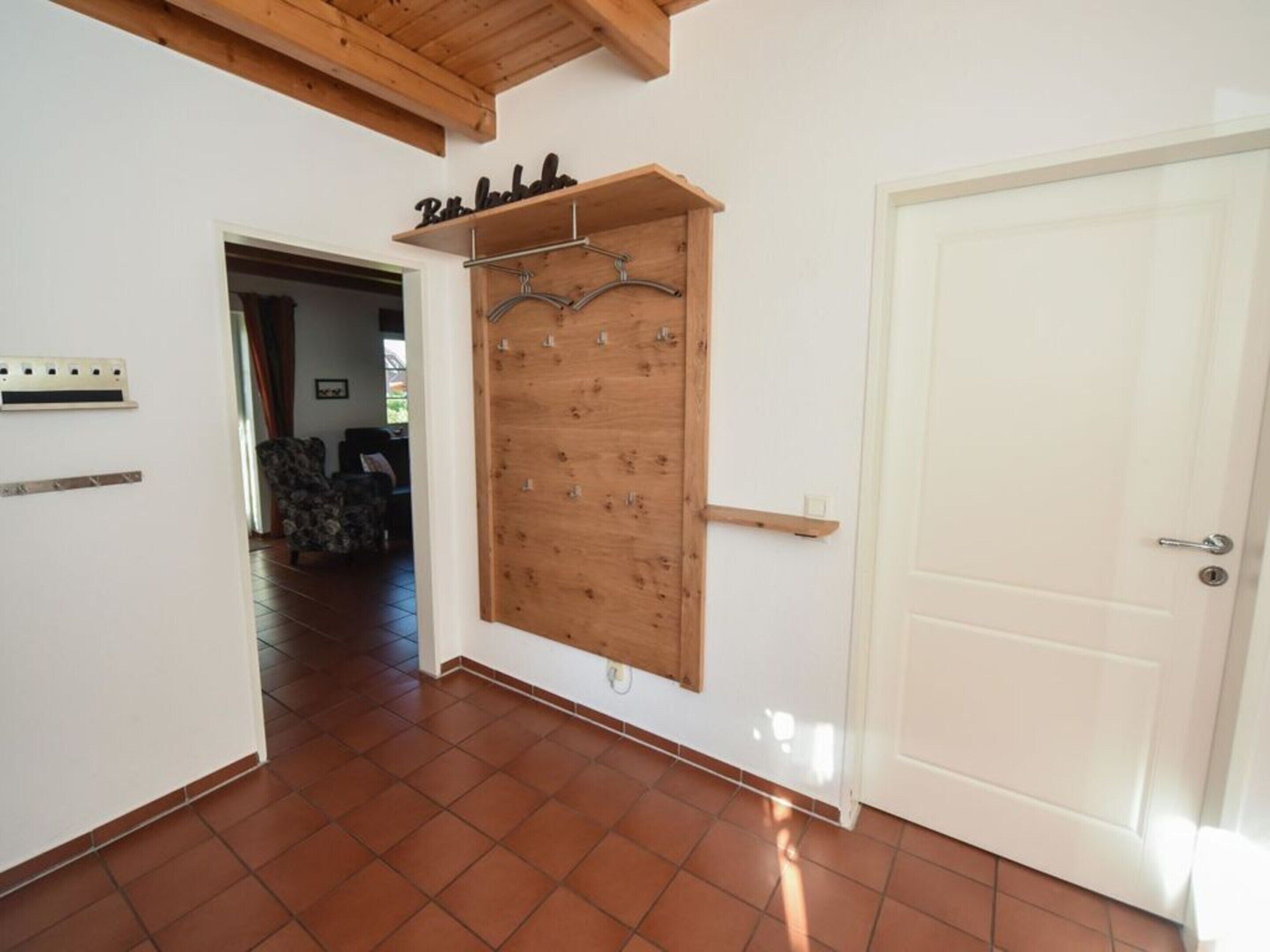 Un couloir avec une porte en bois, un porte-manteau fixé au mur et un sol carrelé.