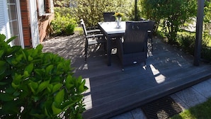 A covered patio with a table and chairs, surrounded by greenery and a brick wall. - Holiday Home Nispel Comfortable Vacation Home (Dornum)