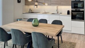 A modern kitchen with a wooden dining table, grey chairs, and a green vase. - Holiday Home in Zeeland With Workation Setup (Wemeldinge)