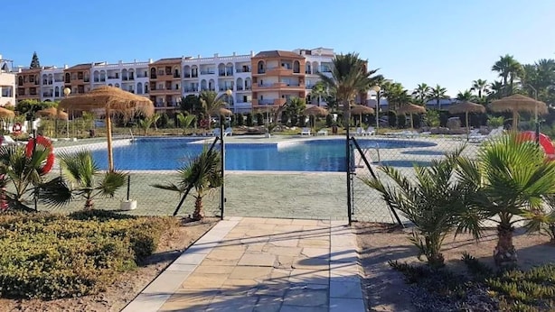 Een resort met een zwembad, palmbomen en meerlaagsgebouwen met balkons.