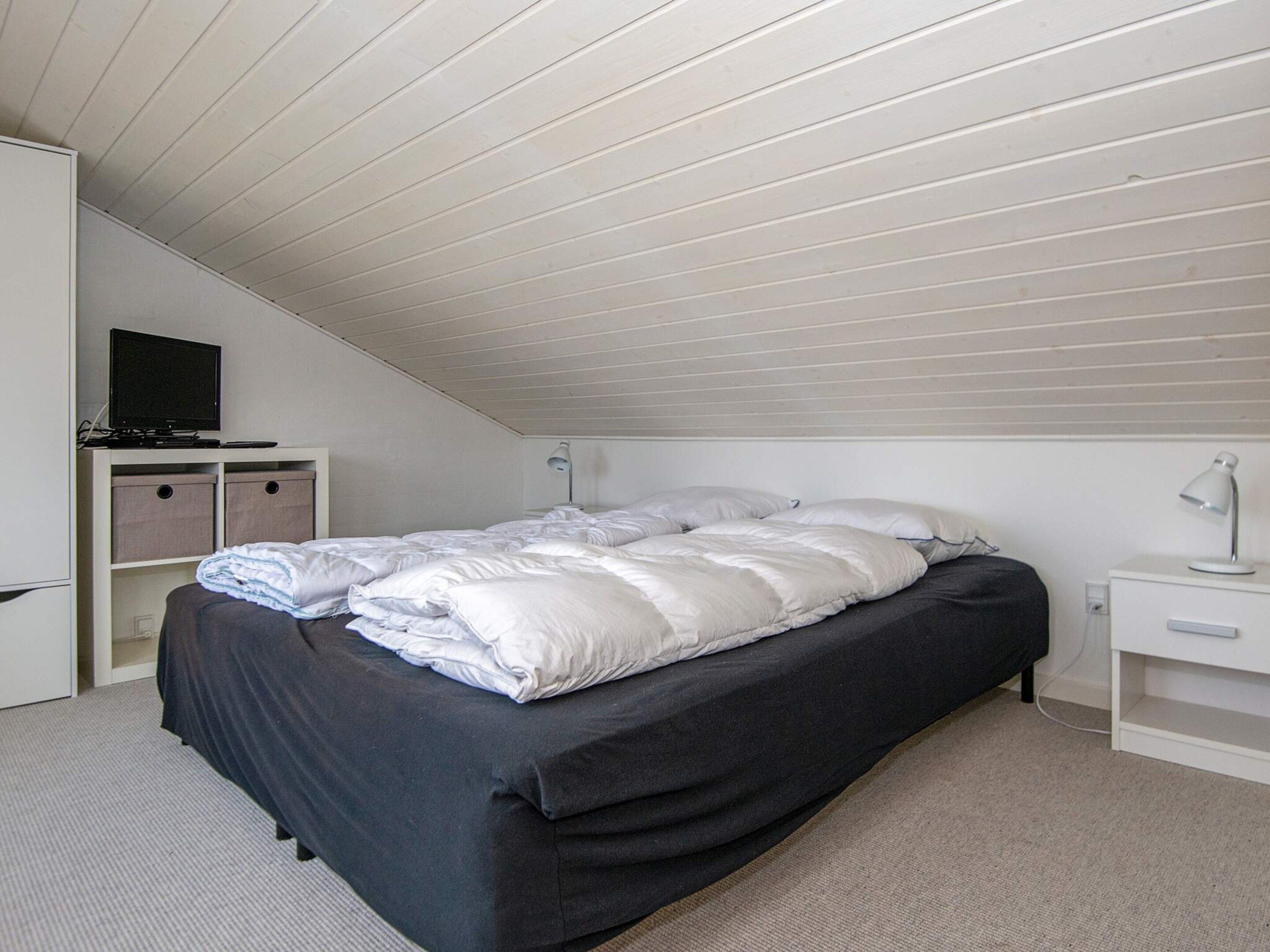 Un dormitorio con cama, escritorio, silla, televisor y armarios.
