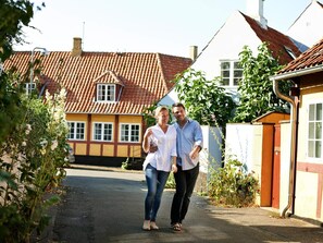 Eine enge Straße mit Häusern an beiden Seiten, darunter ein gelbes Gebäude mit rotem Ziegeldach und ein weißes Gebäude mit roter Tür.
