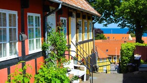 Un bâtiment traditionnel à la façade rouge et jaune, avec un escalier apparent et une vue sur la mer en arrière-plan.