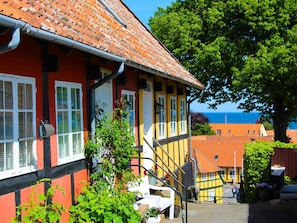 Ein traditionelles Gebäude mit einer roten und gelben Fassade, einer sichtbaren Treppe und Blick auf das Meer im Hintergrund.