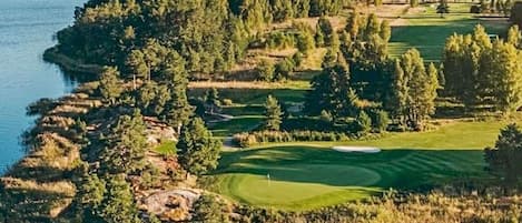 A golf course with a body of water on one side, surrounded by dense forest.