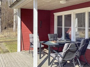 Eine überdachte Terrasse mit Tisch und Stühlen, einem Fenster und einer roten Wand.